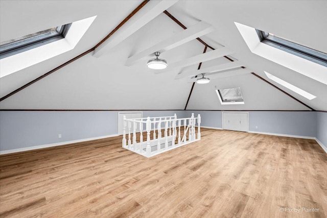 additional living space featuring baseboards, vaulted ceiling with skylight, and wood finished floors