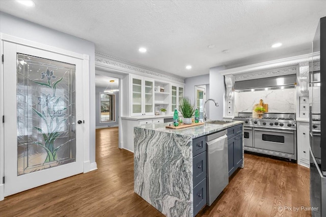 kitchen with light stone countertops, dark wood-style floors, an island with sink, a sink, and appliances with stainless steel finishes