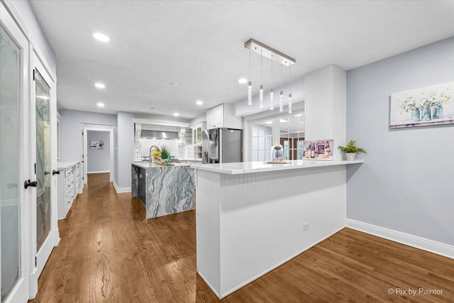 kitchen with light countertops, a peninsula, freestanding refrigerator, dark wood-style floors, and white cabinetry