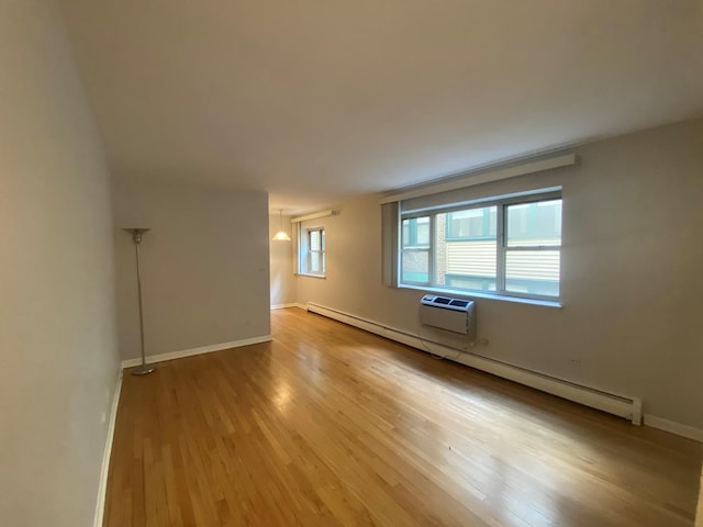 unfurnished room featuring baseboard heating, baseboards, light wood-style floors, and a wall unit AC