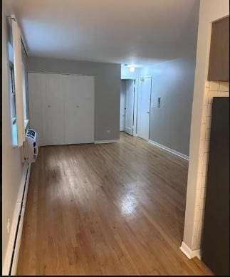 unfurnished living room with baseboards, wood finished floors, and a wall mounted AC