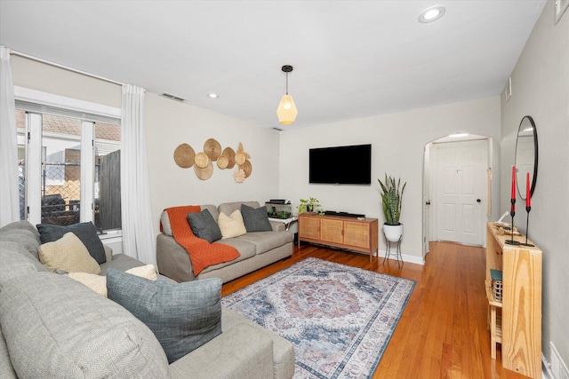 living area with recessed lighting, visible vents, arched walkways, and wood finished floors