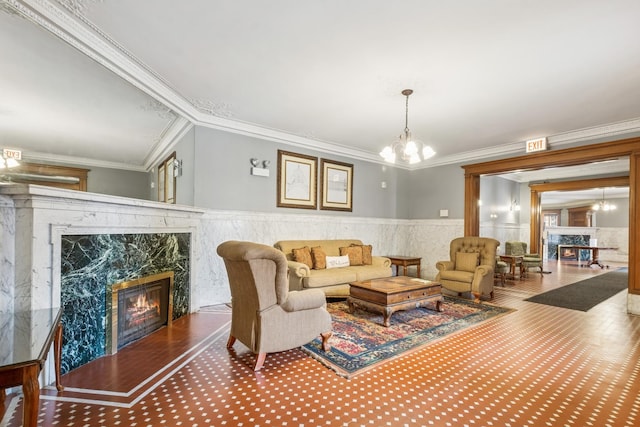 living room with a premium fireplace, an inviting chandelier, ornamental molding, and wainscoting