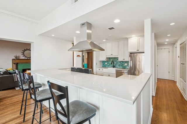 kitchen with wood finished floors, visible vents, island exhaust hood, stainless steel appliances, and a tiled fireplace