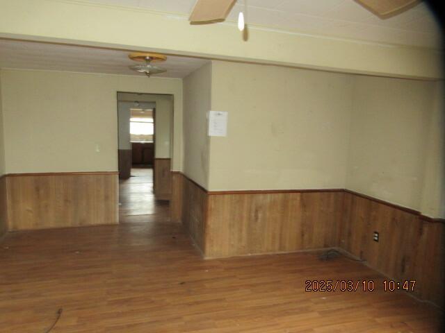 spare room featuring wood finished floors, a ceiling fan, wood walls, and wainscoting