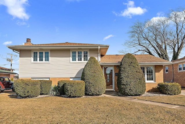 tri-level home featuring a front yard, brick siding, and a chimney