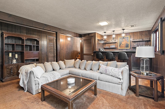 living area featuring visible vents, a textured ceiling, carpet floors, wooden walls, and a dry bar