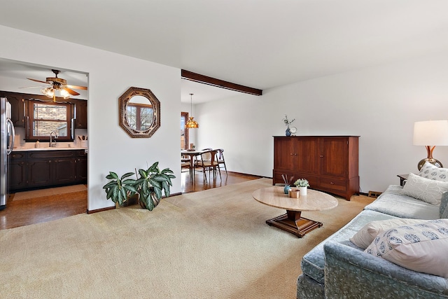 living room with beamed ceiling, baseboards, light colored carpet, and a ceiling fan