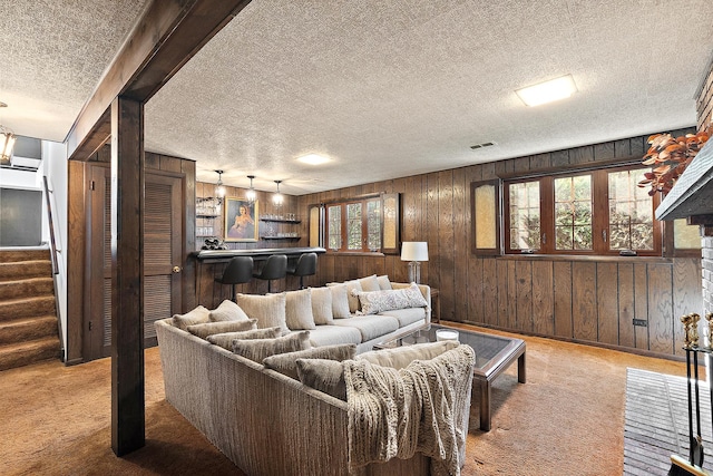 carpeted living room featuring visible vents, stairs, wood walls, a textured ceiling, and a dry bar