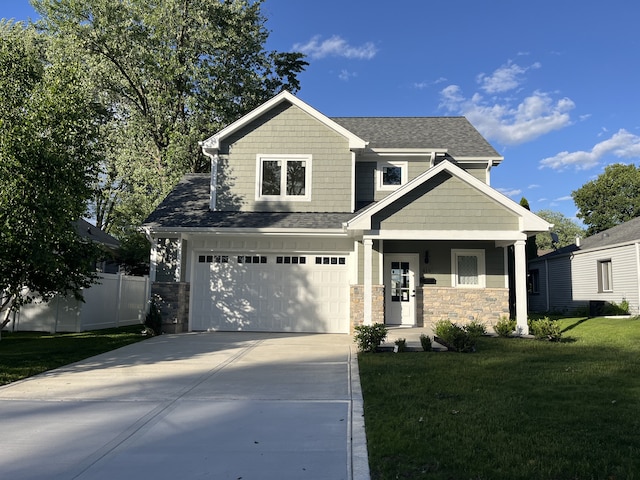 craftsman-style house featuring an attached garage, fence, a front yard, stone siding, and driveway