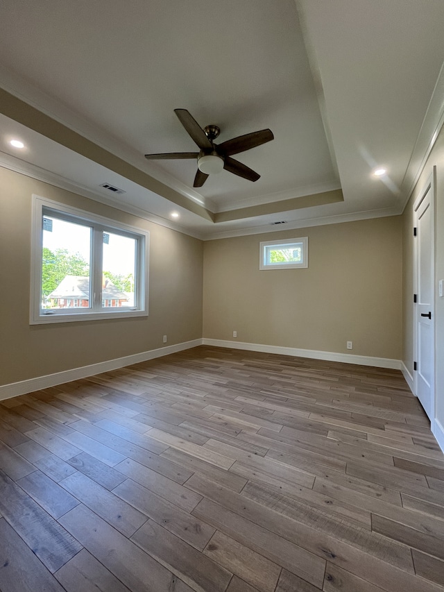 unfurnished room with a tray ceiling, a healthy amount of sunlight, wood finished floors, and crown molding