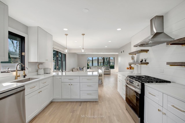 kitchen with a sink, open shelves, open floor plan, appliances with stainless steel finishes, and wall chimney range hood