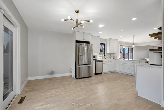 kitchen featuring light wood-type flooring, stainless steel appliances, decorative light fixtures, and light countertops