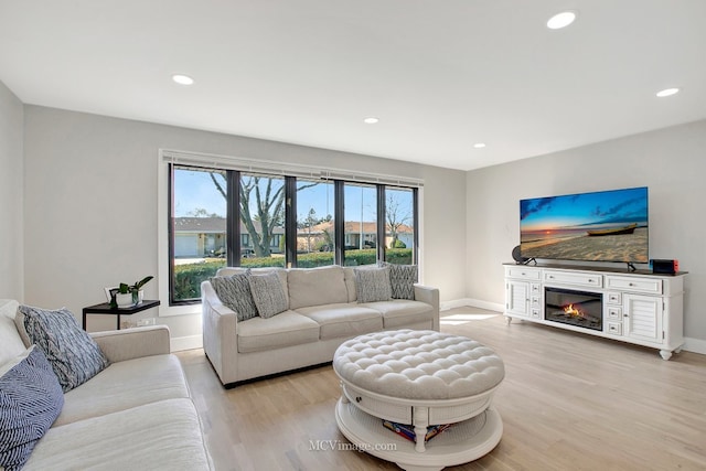 living room with a glass covered fireplace, recessed lighting, light wood-type flooring, and baseboards