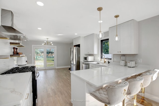 kitchen with a breakfast bar, light wood-style flooring, a sink, appliances with stainless steel finishes, and wall chimney range hood