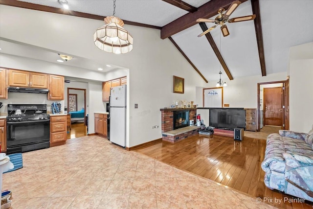 kitchen with under cabinet range hood, black gas range, open floor plan, a fireplace, and freestanding refrigerator