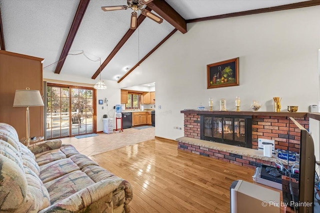 living room featuring light wood-type flooring, beamed ceiling, a textured ceiling, a brick fireplace, and ceiling fan