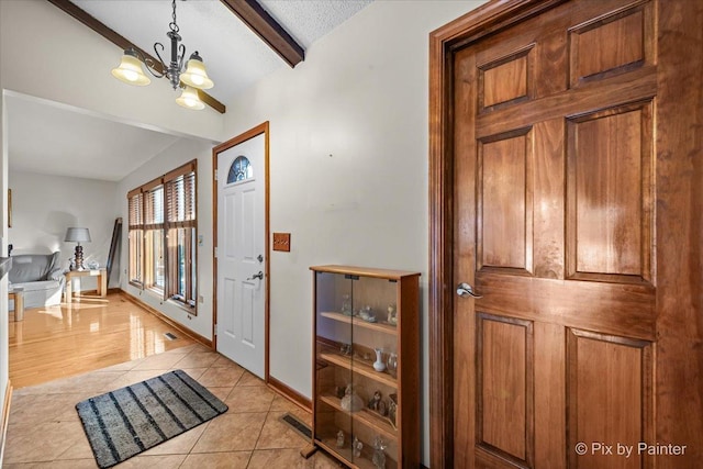 entrance foyer with beam ceiling, a textured ceiling, an inviting chandelier, light tile patterned flooring, and baseboards