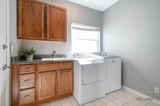 clothes washing area featuring a sink, cabinet space, light tile patterned floors, baseboards, and washing machine and clothes dryer