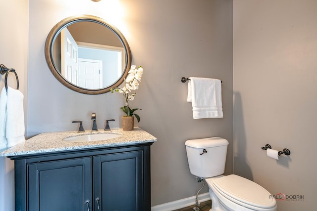 half bathroom featuring baseboards, toilet, and vanity