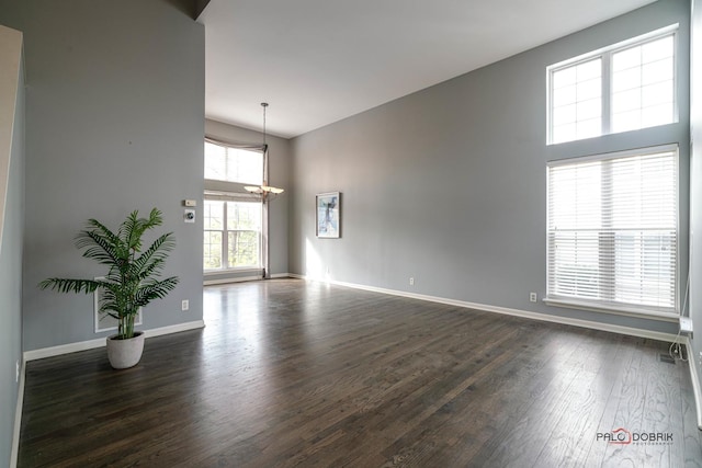 spare room with dark wood-style floors, an inviting chandelier, a high ceiling, and baseboards