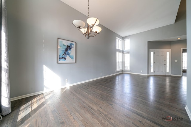 spare room with baseboards, dark wood-style flooring, a towering ceiling, and a chandelier