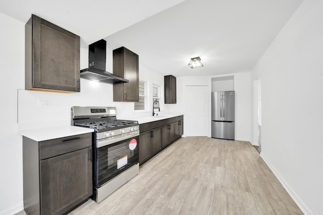 kitchen featuring a sink, stainless steel appliances, light countertops, light wood-style floors, and wall chimney exhaust hood