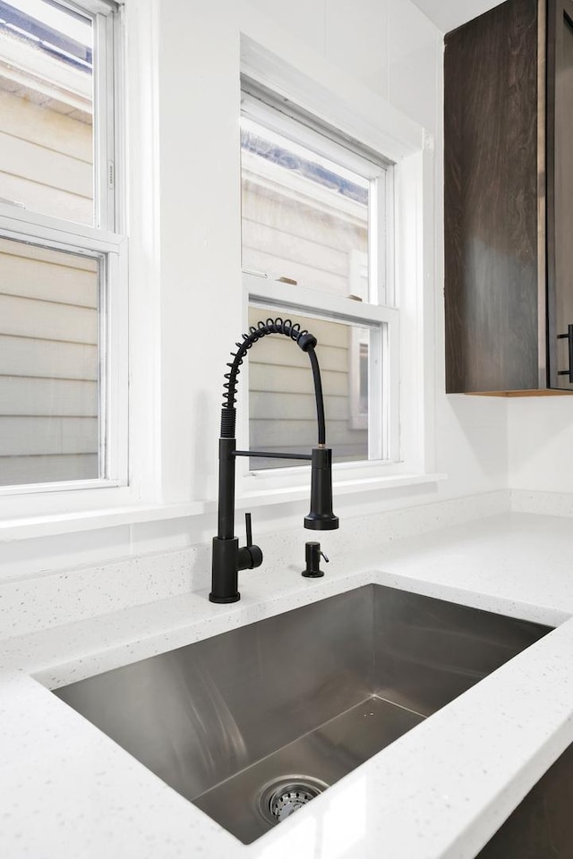 details with a sink, light stone counters, and dark brown cabinets