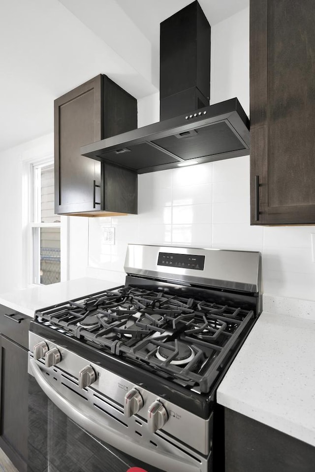 kitchen with decorative backsplash, dark brown cabinetry, wall chimney range hood, and stainless steel gas range oven