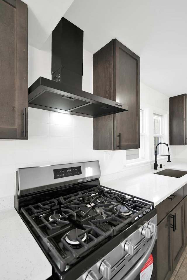 kitchen featuring a sink, dark brown cabinetry, stainless steel range with gas stovetop, and wall chimney range hood