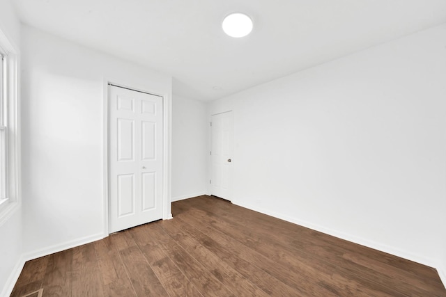 unfurnished bedroom with dark wood finished floors, a closet, and baseboards