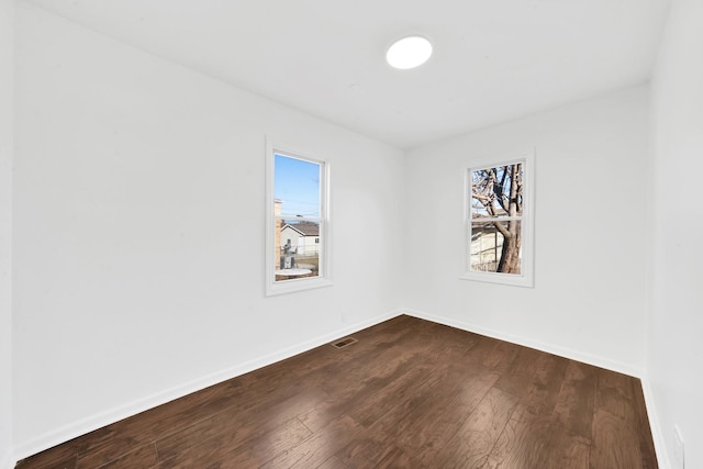 empty room featuring dark wood finished floors, baseboards, and visible vents