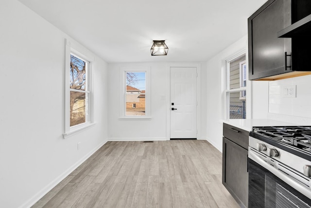 kitchen featuring baseboards, stainless steel gas stove, light wood-style flooring, and light countertops