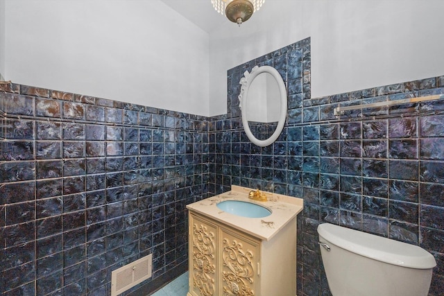 half bathroom featuring visible vents, toilet, tile walls, and vanity