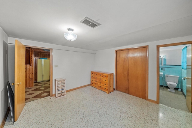 bedroom with tile patterned floors, visible vents, ensuite bathroom, freestanding refrigerator, and baseboards