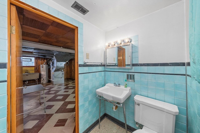 bathroom featuring visible vents, a wainscoted wall, toilet, a sink, and water heater