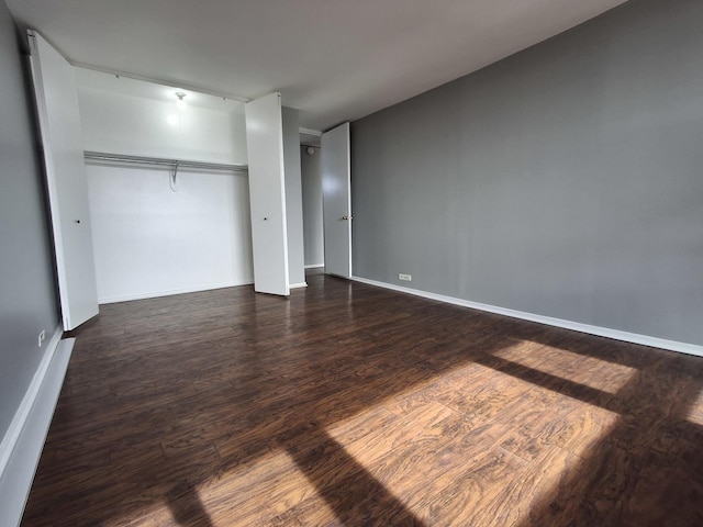 unfurnished bedroom with a closet, baseboards, and dark wood-style flooring