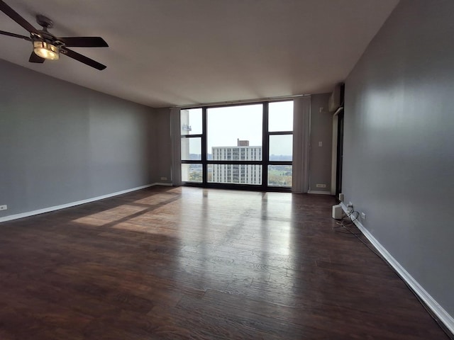 spare room featuring a wall of windows, baseboards, wood finished floors, and a ceiling fan