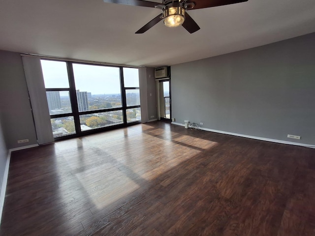 unfurnished room featuring an AC wall unit, a wall of windows, baseboards, ceiling fan, and dark wood-style flooring