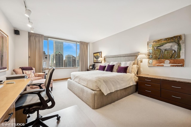 bedroom with a view of city, rail lighting, and light carpet