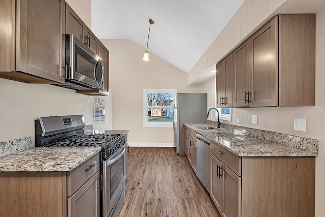 kitchen with a sink, stainless steel appliances, light wood-style floors, baseboards, and vaulted ceiling