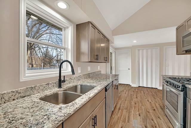 kitchen with light wood finished floors, light stone countertops, lofted ceiling, appliances with stainless steel finishes, and a sink