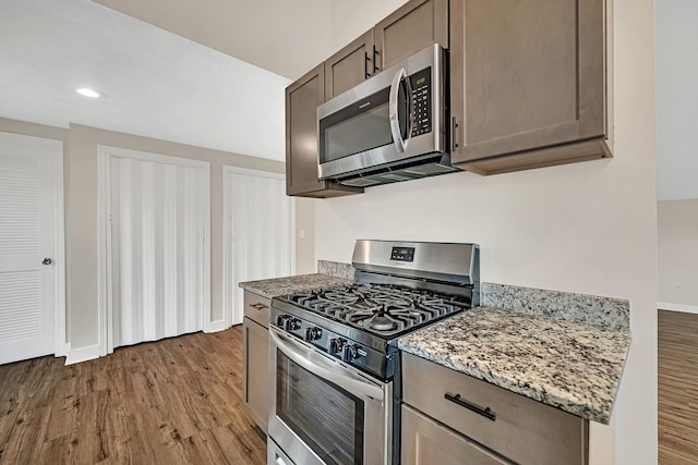 kitchen featuring light stone counters, baseboards, stainless steel appliances, and light wood-style floors