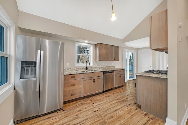 kitchen featuring lofted ceiling, light stone counters, light wood-style floors, stainless steel appliances, and a sink