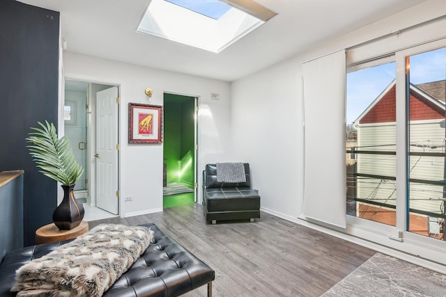 living area featuring a skylight, wood finished floors, visible vents, and baseboards