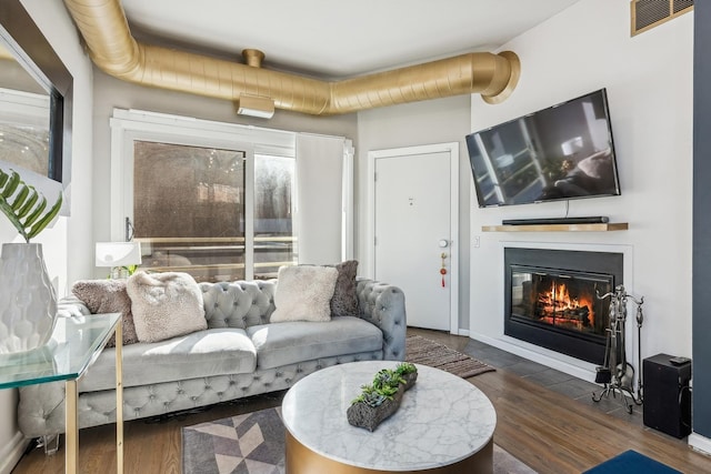 living area featuring visible vents, wood finished floors, and a glass covered fireplace