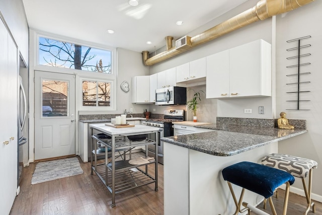 kitchen featuring visible vents, white cabinetry, appliances with stainless steel finishes, a peninsula, and dark wood-style flooring