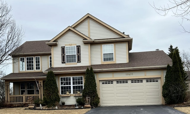 traditional home with covered porch, a garage, driveway, and a shingled roof