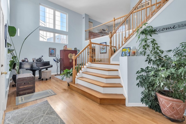 staircase featuring baseboards, wood finished floors, and a towering ceiling