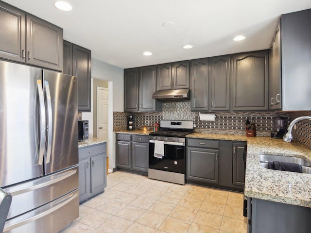 kitchen featuring a sink, light stone counters, under cabinet range hood, appliances with stainless steel finishes, and decorative backsplash